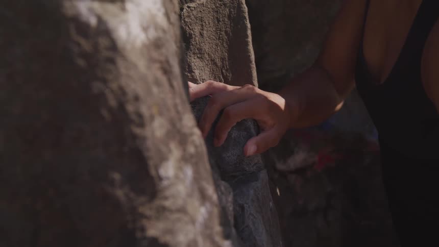 A woman reaches up and grabs a handhold as she climbs a sheer rock