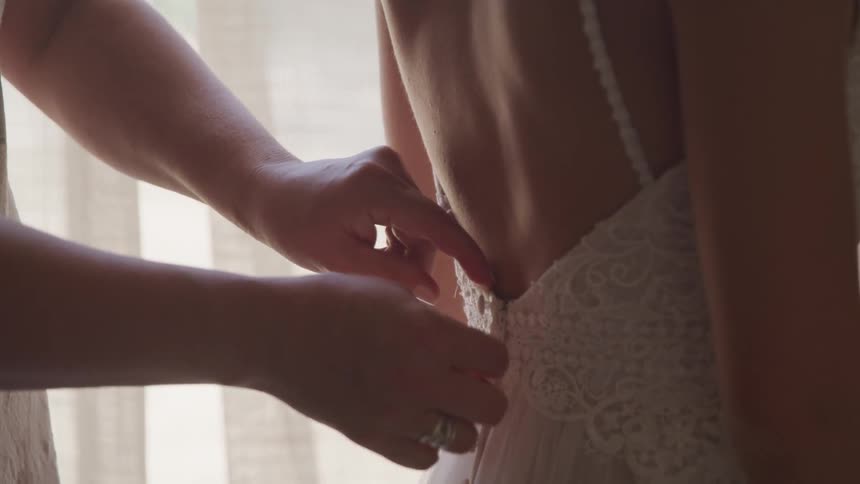 A woman buttons the back of a wedding gown