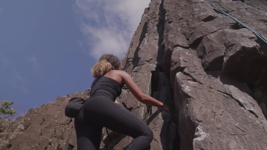 A black woman climbing rocky cliff