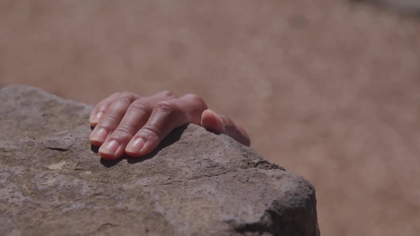 A climbers hand reaches up and grabs onto a rock ledge