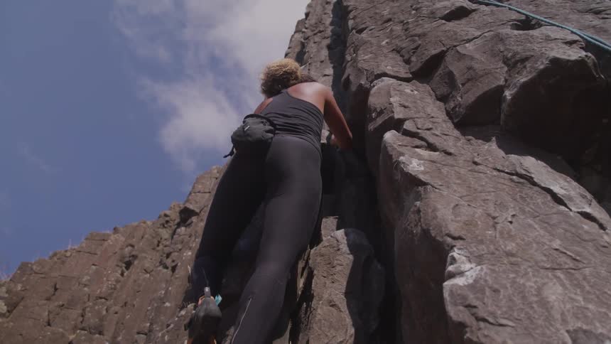 A woman rock climbs outdoors on basalt