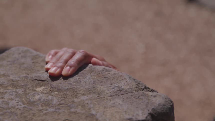 A black female placing her hand on a rock outside