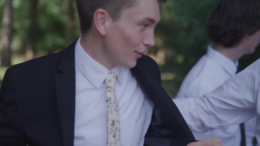 Man wearing a suit adjusts his jacket as he talks to another man