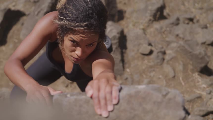 A woman reaches to pull herself up while rock climbing