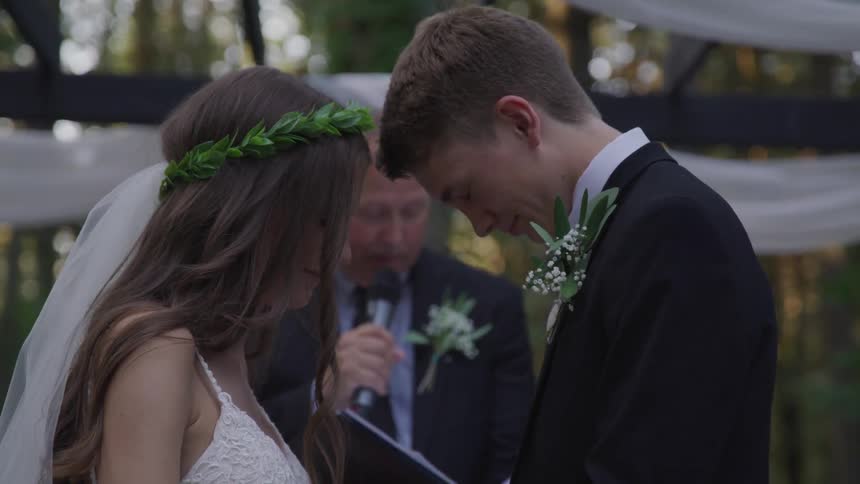 A bride and groom face each other with heads bowed during their outdoor wedding ceremony