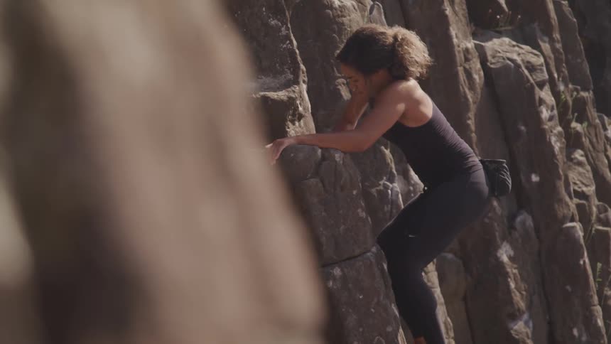A woman reaches up to pull herself forward rock climbing