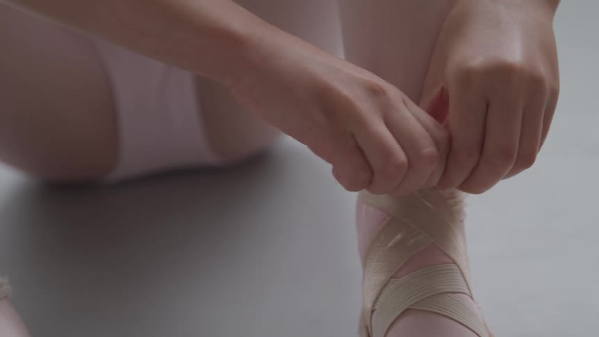 A dancer sitting on the floor tying her ballet shoes