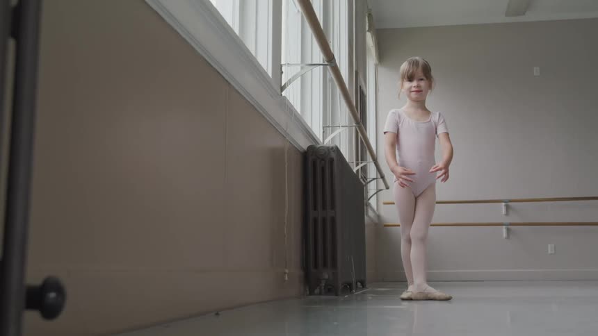 Little ballerina does a ballet position next to the handrail in the ballet studio