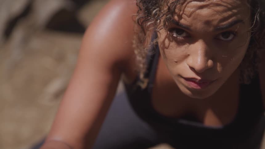 A woman looking up at the camera while climbing a rock wall