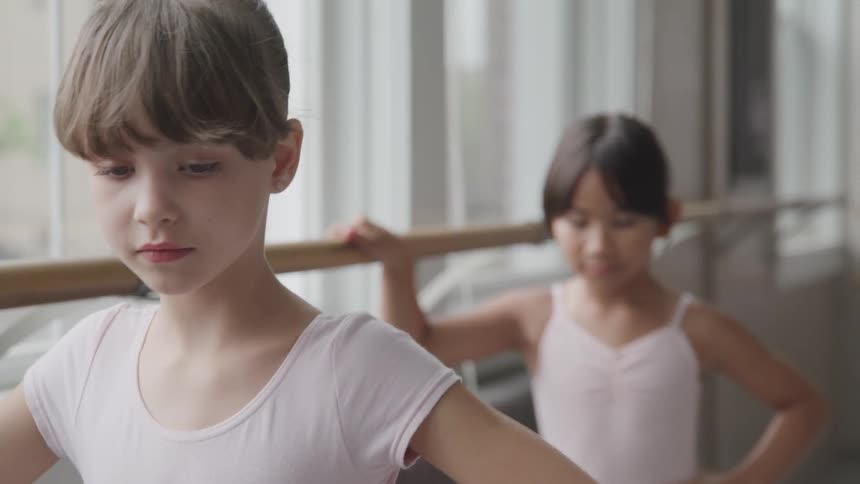Two girls practice plie at a ballet barre in a dance studio