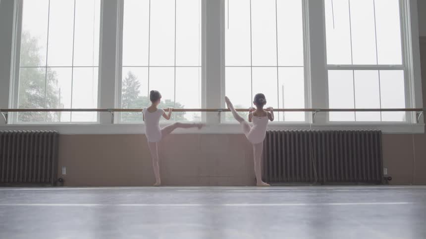 Two ballerinas holding handrail warms up for dancing in the ballet studio