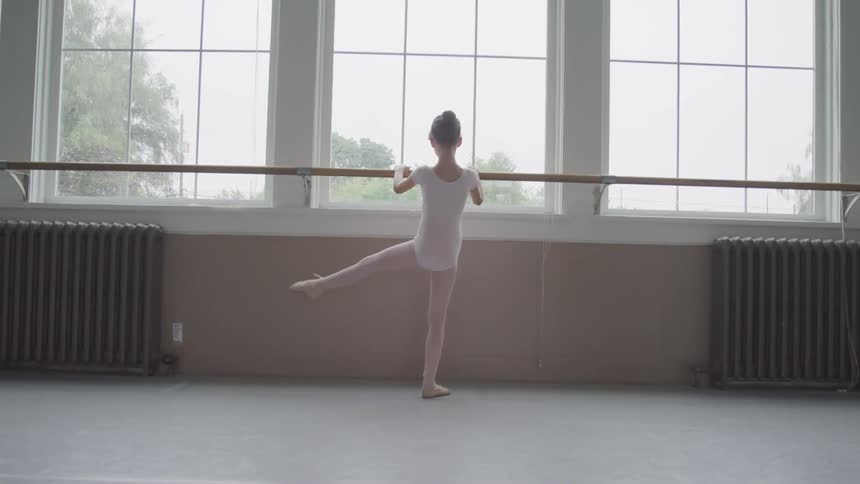 A girl is doing ballet in a room indoors