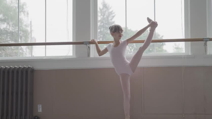 Little ballerina holding handrail warms up for dancing in the ballet studio