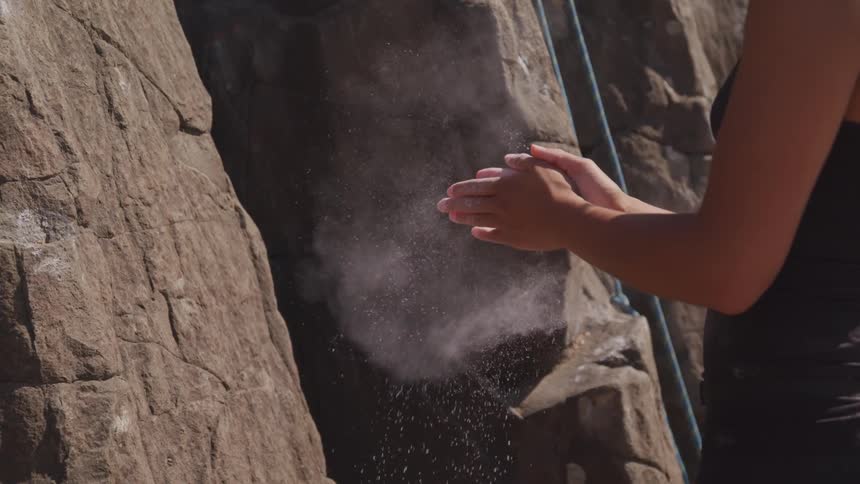 A woman rubs chalk on her hands before mountain climbing
