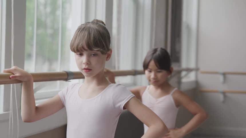 Two little ballerinas holding handrail warm up for dancing in the ballet studio