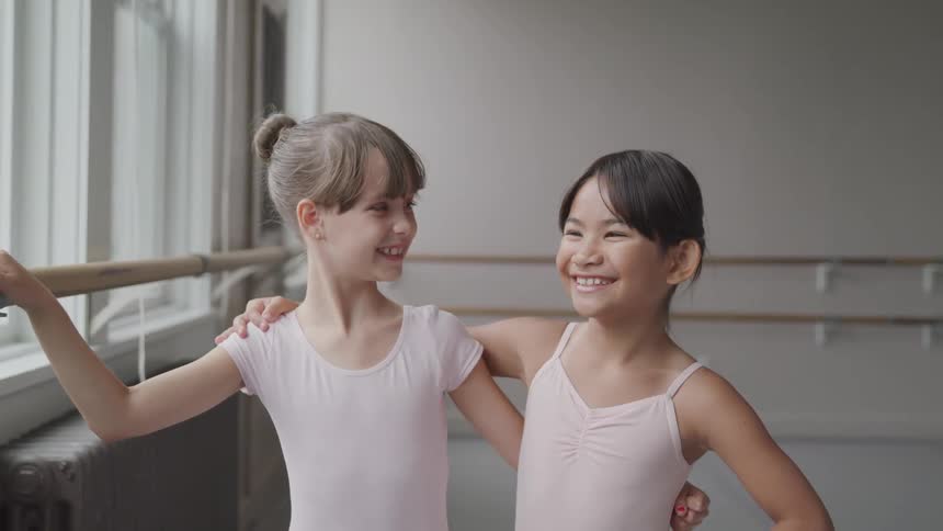 Two young ballet dancers hug and smile at each other