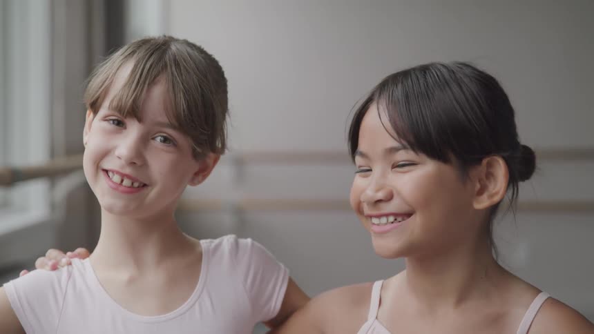 Two ballerinas look at each other and smile and then smile for the camera