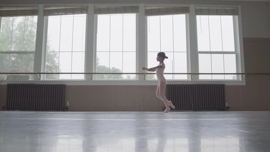 Young ballerina dances across the room near the windows