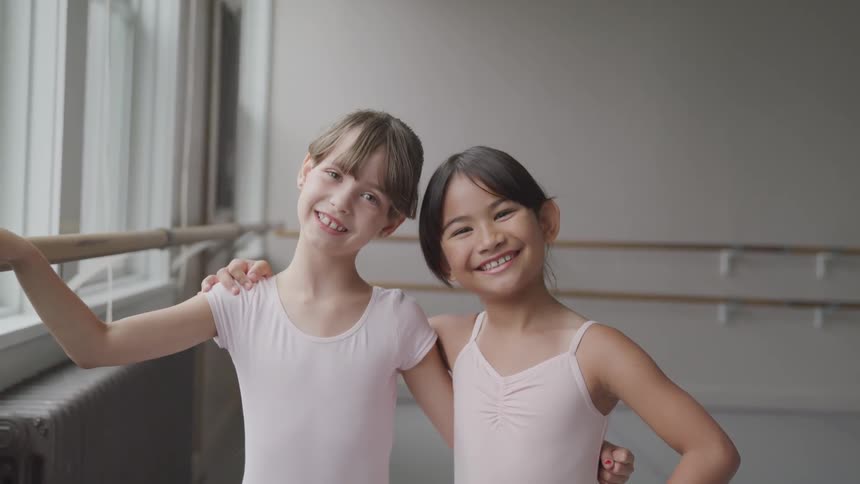 Two little girls in a dance studio smile and pose with their arms around each other