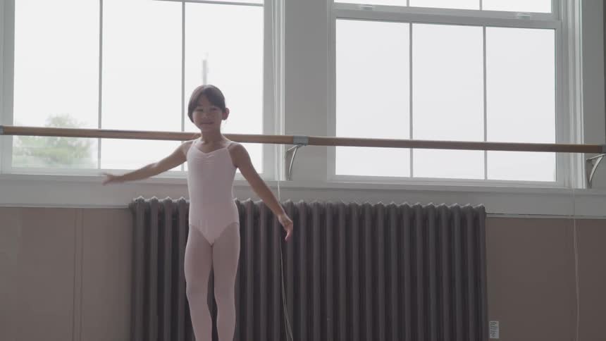 Little ballerina holding handrail warms up in the ballet studio