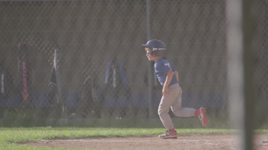 A boy hitting a ball off a tee and running towards first base