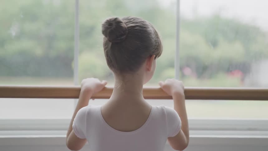 A girl in front of a window holding on to a ballet barre