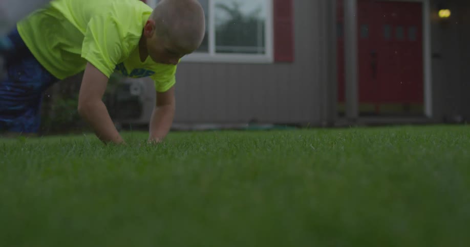 A boy runs over to catch a baseball on the grass