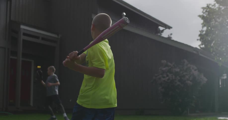 Children play baseball outside of a house during the day