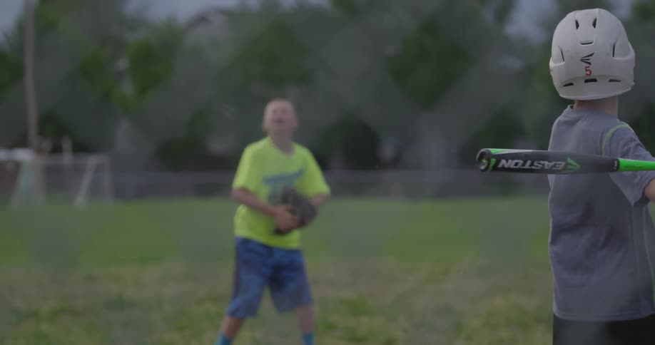 Two boys in a field practicing pitching and batting