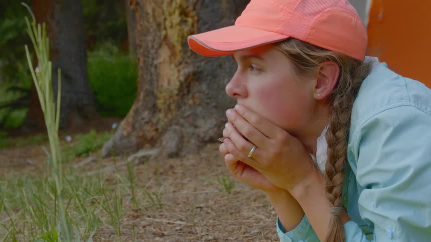 Blonde girl wearing red cap looks around next to the tent in the camp