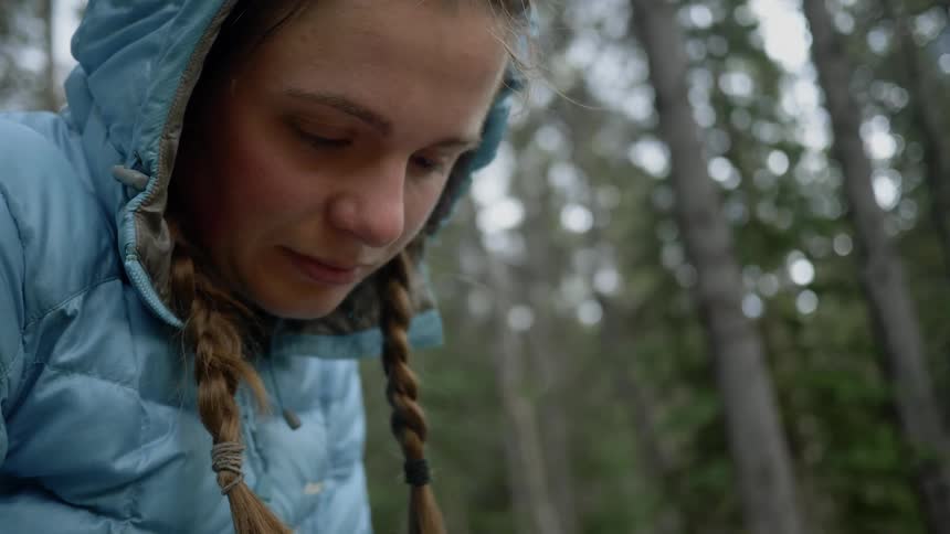 A girl sits in the woods with the hood of her jacket up