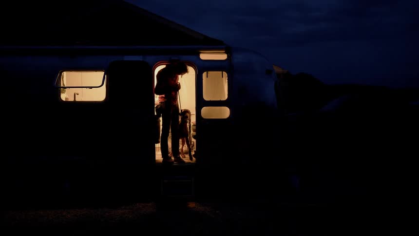 A man at the door of a camper with a dog on a leash