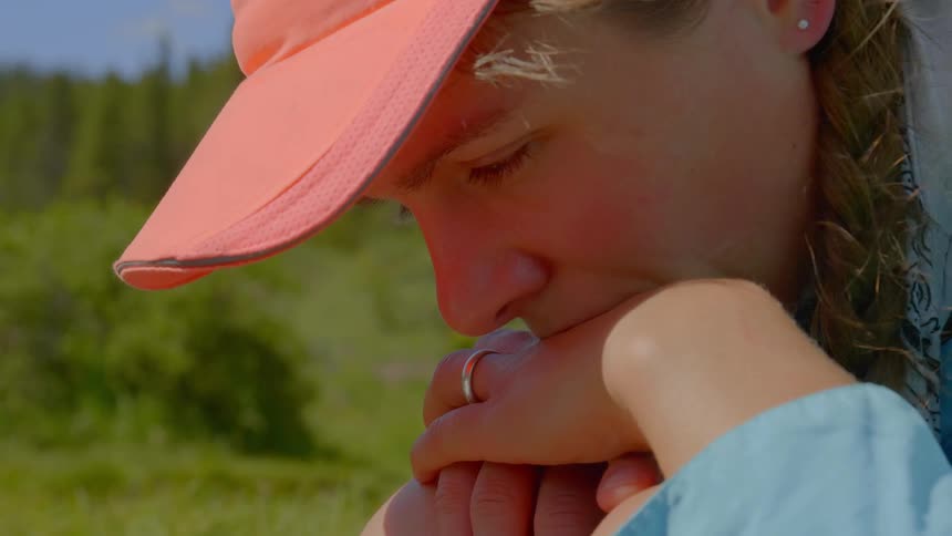 Sad woman wearing a pink hat with her chin on her hands in a field