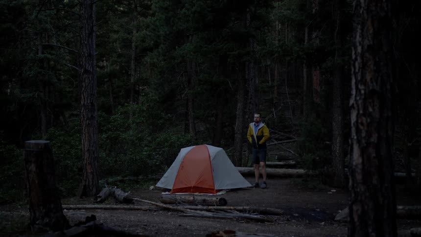 Man puts a vest on as he stands near a tent then he walks away
