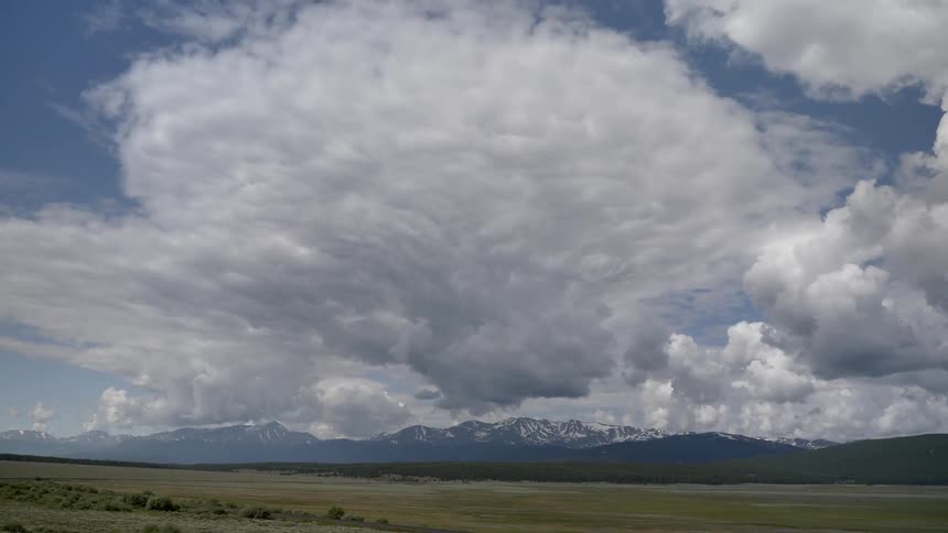 Large white clouds hang in a blue sky over plains and mountains