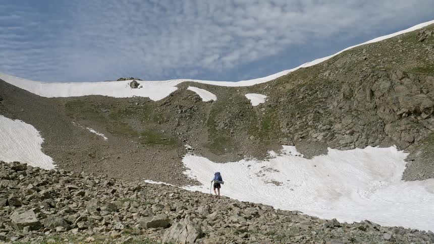Woman uses trekking poles as she walks on a rocky trail near a mountain