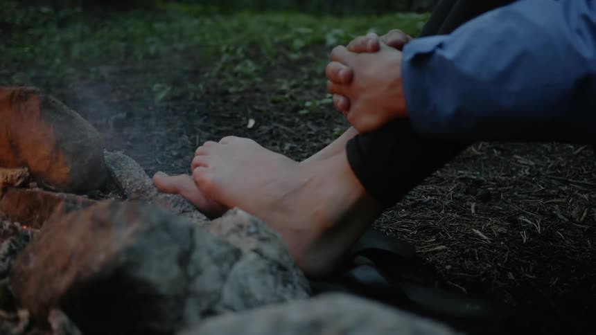 Someone sits with their feet on a camp fires surrounding ring of rocks