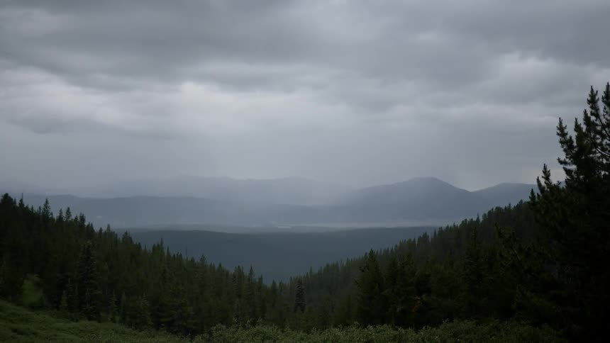 Within an expansive mountain range a valley is filled with trees under a cloudy sky
