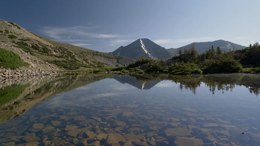 A clear lake with a rock bed surrounded by mountains and greenery