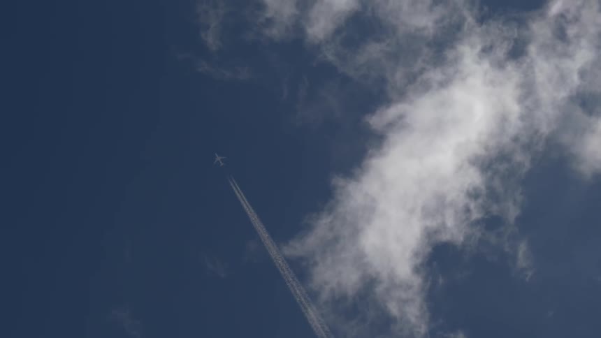 A jet flies through the sky far above us leaving a contrail in its wake