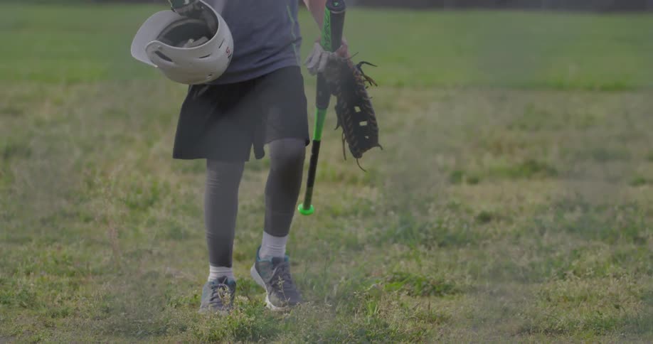 A boy picks up a baseball helmet while walking on a field