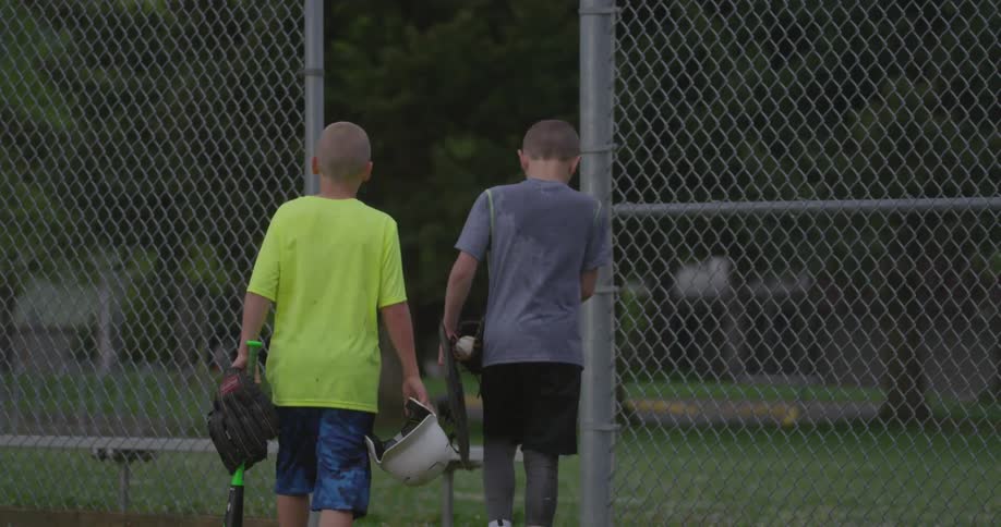 Two boy with baseball gear walk away from a playing field