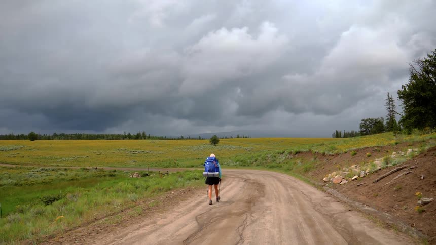 Woman carrying backpack walks on the dirt road in the plains