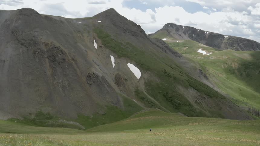 A person walks across a field towards a hill