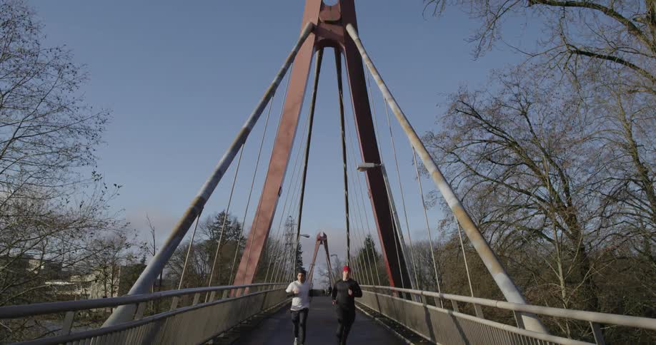 Two men jog over a bridge on a cold day