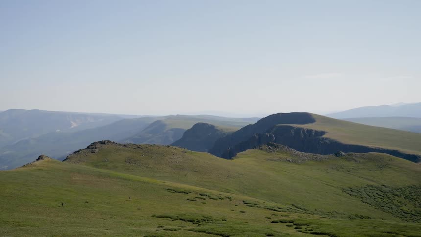 Grass covers a group of hills that are within an expansive mountain range
