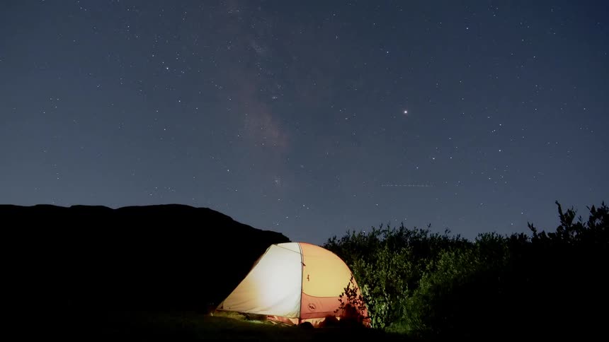 A time lapse of a brightly illuminated camping tent shows the stars in the night sky rotating above