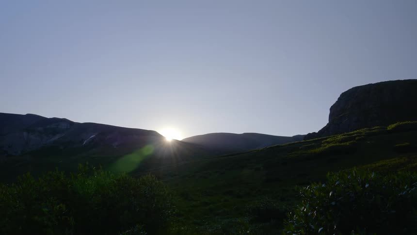 Sun goes down behind the mountains with the view of cloudless sky