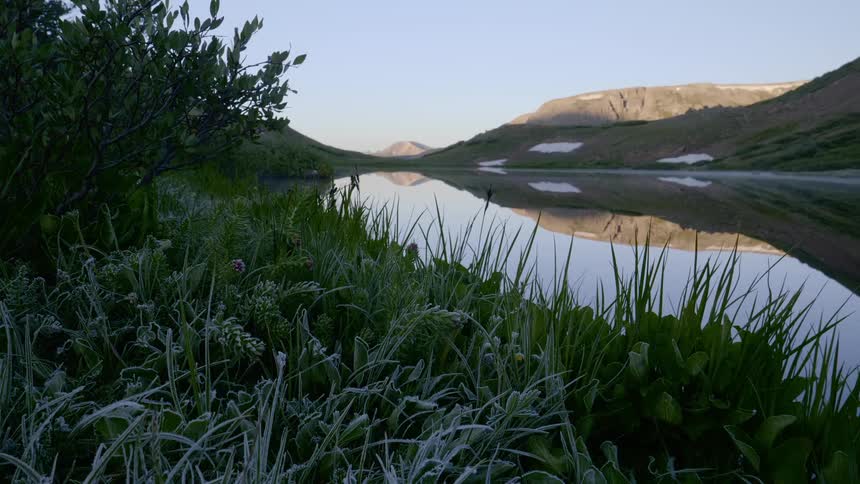 A calm river next to hills green grass and mountains