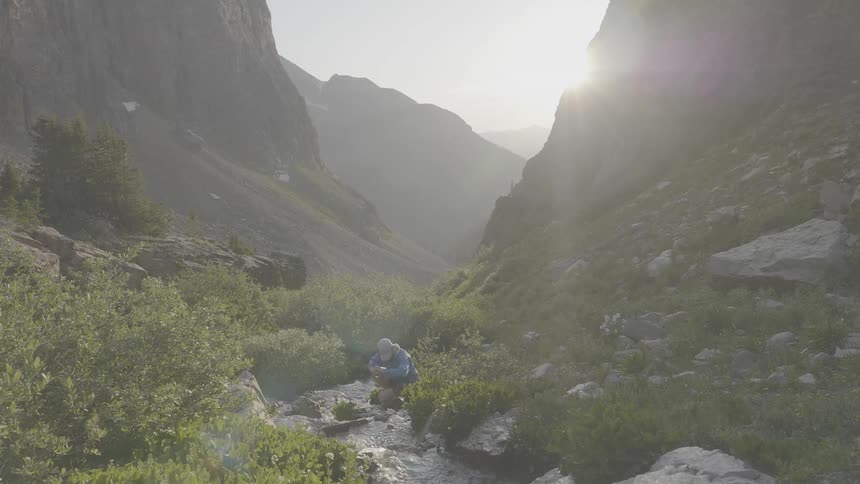 Man fills water bottles in the creek then walks away as birds fly around
